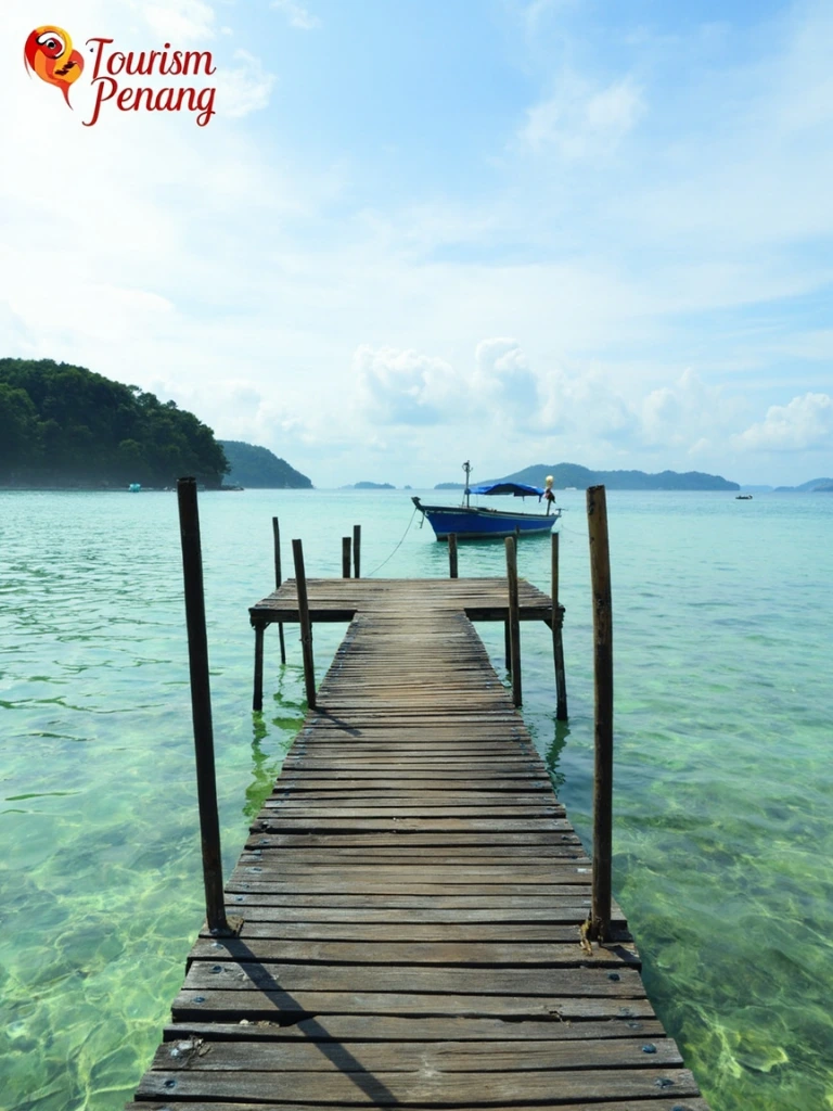 A wooden jetty on Pulau Aman with a single blue fishing boat and clear turquoise water.